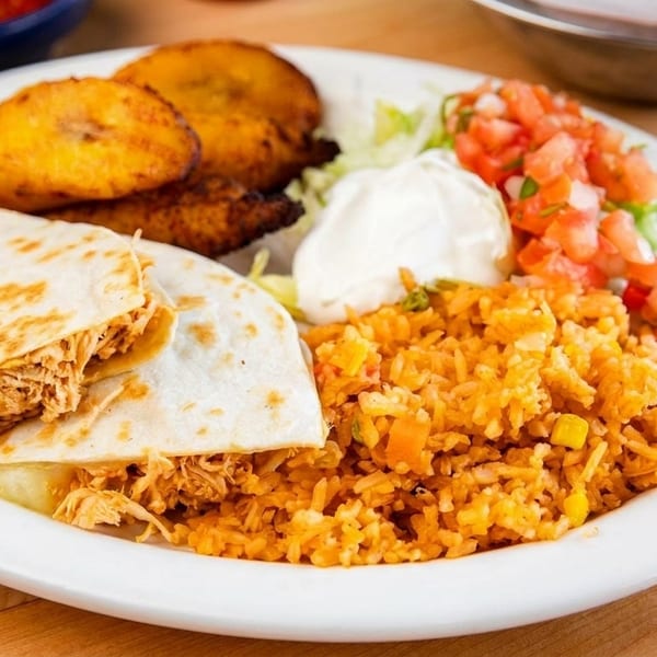 A white plate with chicken quesadillas, yellow rice, fried plantains, sour cream, and pico de gallo.
