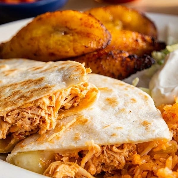Chicken quesadilla with rice, plantains, sour cream, and pico de gallo on a white plate.