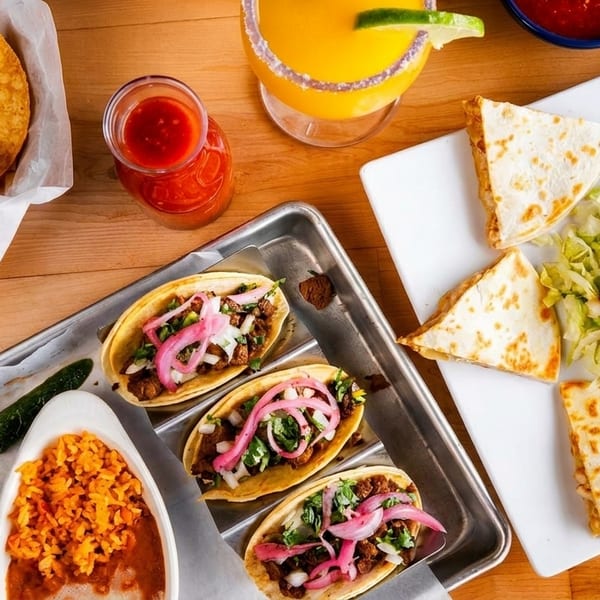 Overhead view of a Mexican feast with tacos, quesadillas, rice, beans, chips, salsa, and a margarita.