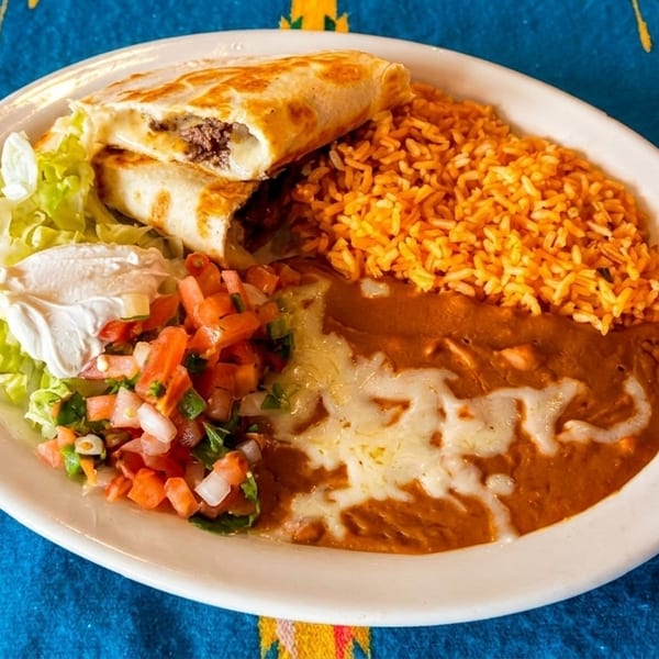 A plate of Mexican food with two burritos, rice, refried beans, lettuce, sour cream, and pico de gallo.