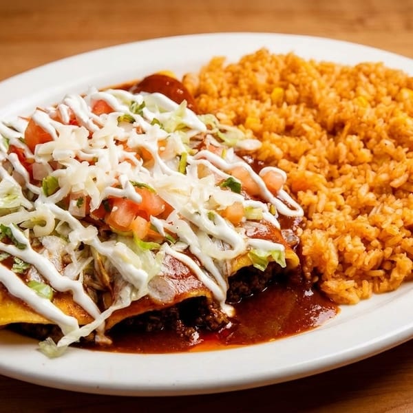 Three enchiladas topped with sour cream, lettuce, tomatoes, and cheese, served with a side of Spanish rice.