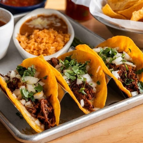 Three birria tacos with cilantro and onions, served with consommé, rice, beans, and chips.