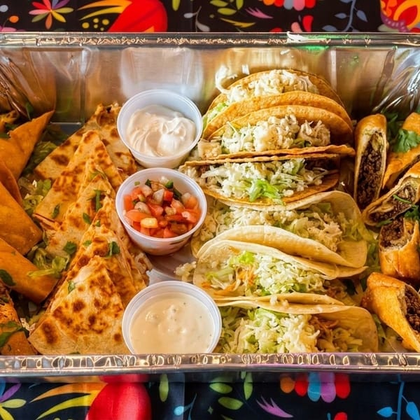 A catering tray filled with tacos, quesadillas, taquitos, and egg rolls, with salsa and sour cream.