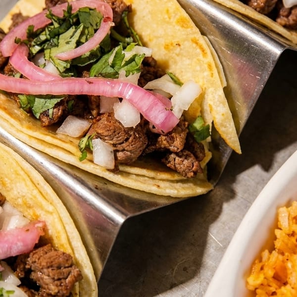 Three street tacos with steak, cilantro, onions, and pickled red onions, served with rice and beans.